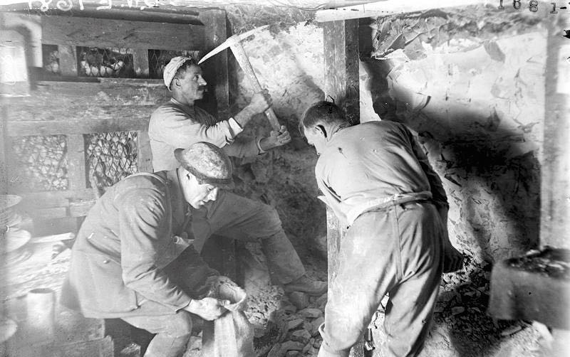 Tunnellers at work in a tunnel. A men is loading a bag with rubbles from the excavation work